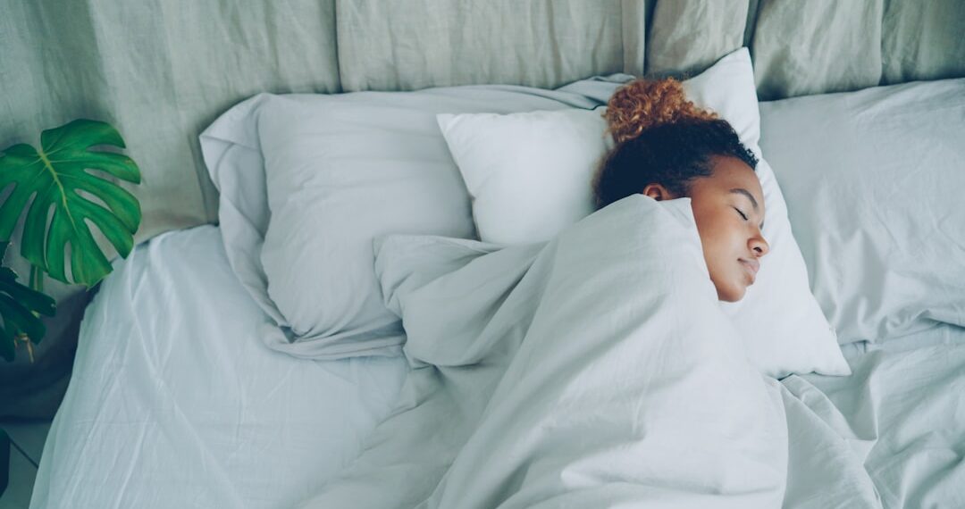 Young African American woman is sleeping in comfortable bed under warm blanket having rest on beautiful linen. Comfort, resting people and bedroom concept.
