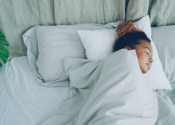 Young African American woman is sleeping in comfortable bed under warm blanket having rest on beautiful linen. Comfort, resting people and bedroom concept.